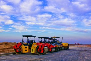 Vibrant road rollers parked on a construction site under a bright blue sky.