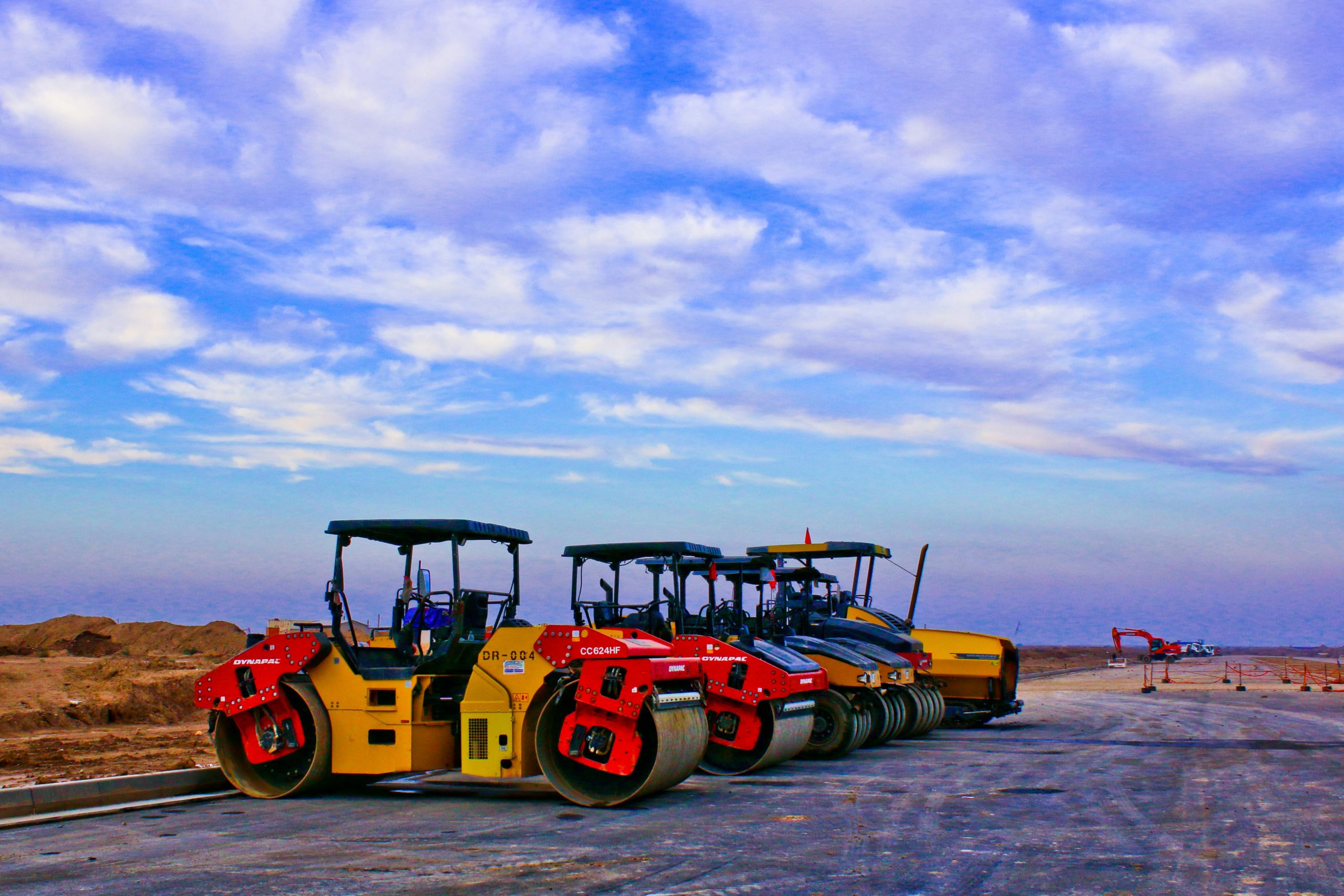 Vibrant road rollers parked on a construction site under a bright blue sky.